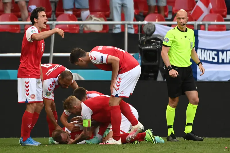 Soccer Players in Red and White Celebrate a Goal As Teammates Pile on a Prone Teammate on the Field with a Neon clad Referee Watching Nearby  Aleumumnews