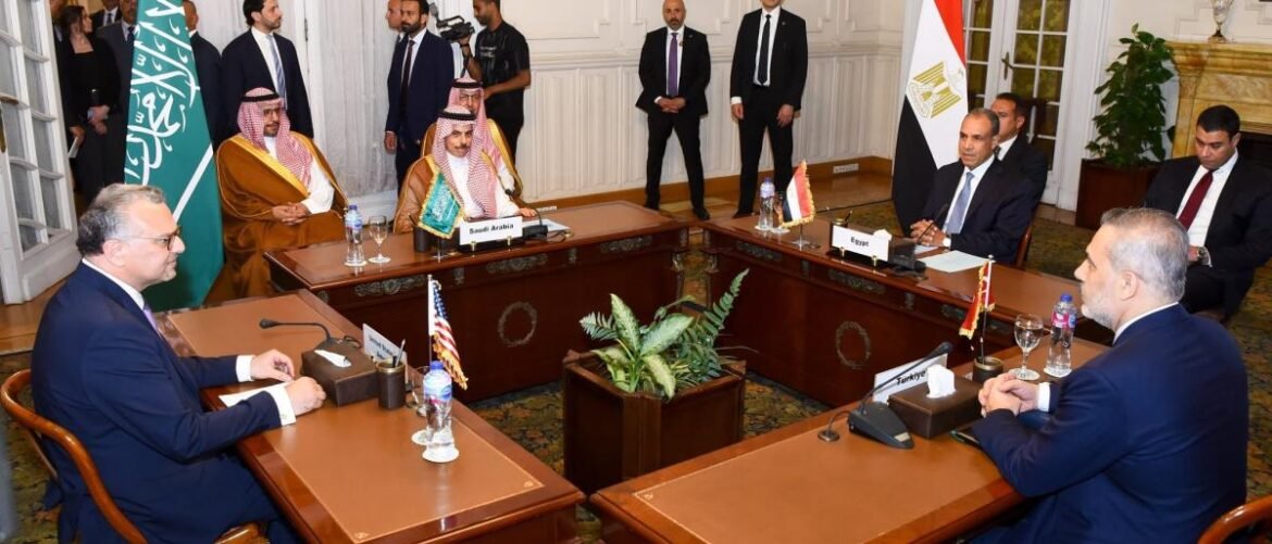Diplomatic leaders sit across from each other at a formal U-shaped conference table with national flags in the room.
