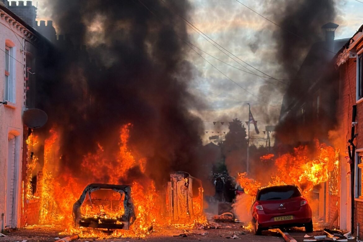 Street engulfed in flames with thick black smoke and burning vehicles on a residential avenue.