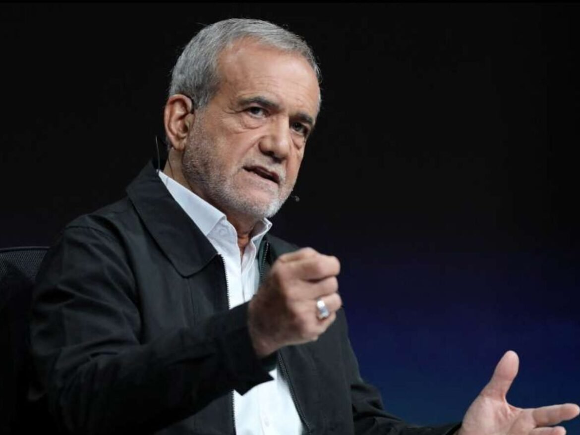 Older man with gray hair and stubble, wearing a white shirt and dark jacket, speaking and gesturing with his hand on a dark stage backdrop.