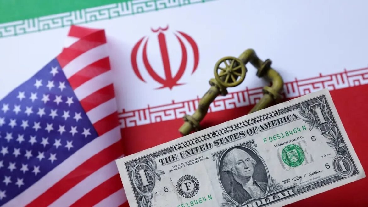 Close-up of a US flag and Iranian flag with a one-dollar bill and an old brass key/lock wheel resting between them.