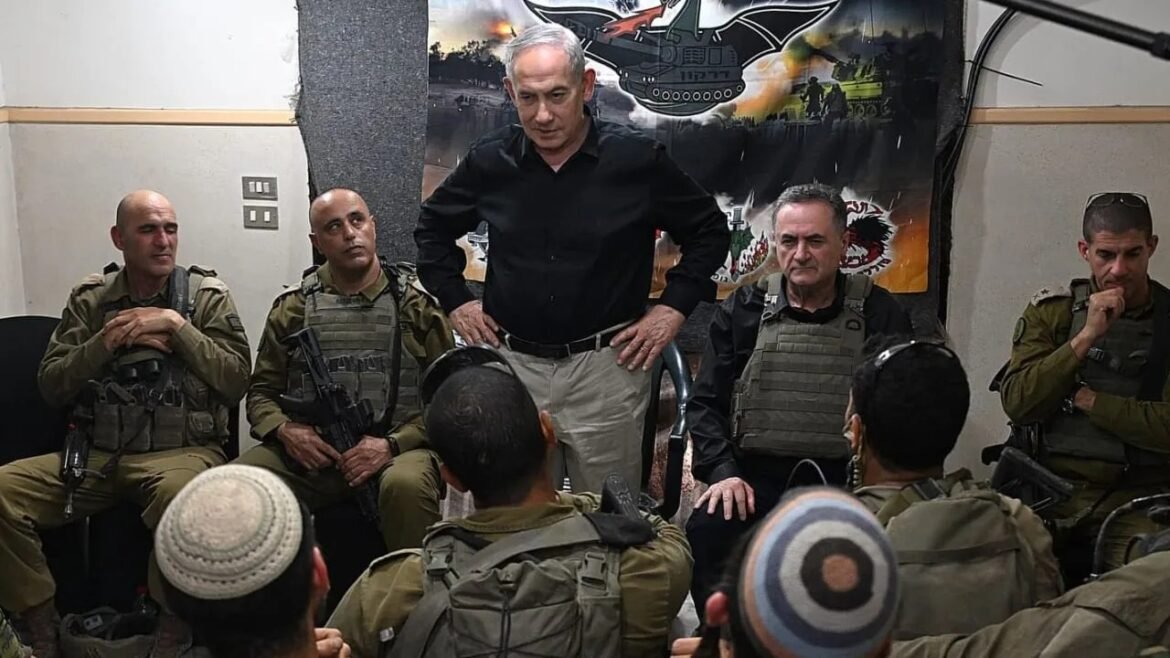 A man in a black shirt speaks to seated soldiers in tactical vests during a briefing, with a military banner in the background behind them.