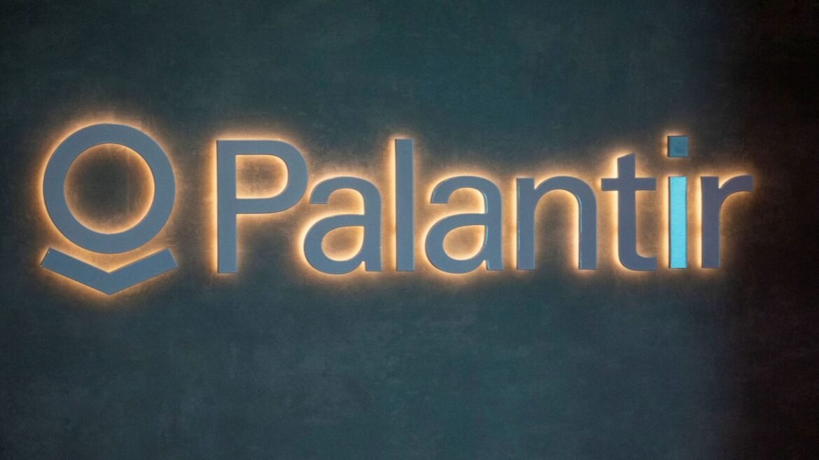 Backlit Palantir sign: blue logo and wordmark on a dark wall.
