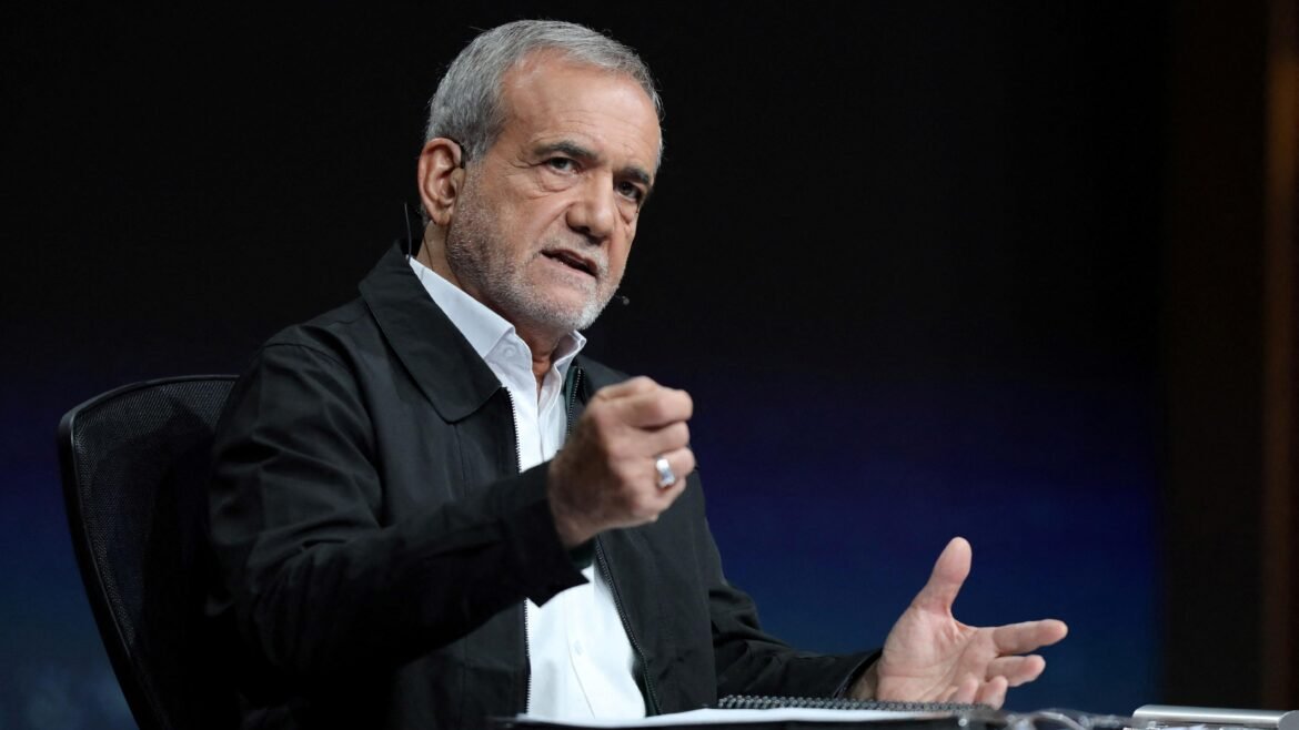 Older man with gray hair and stubble speaks, wearing a white shirt and black jacket, gesturing with his hands during a talk on a dark stage.