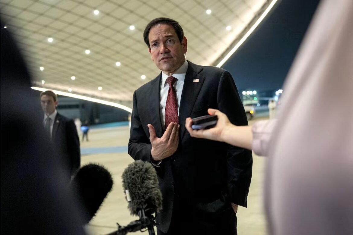 Politician in a dark suit and red tie speaks to reporters at an airport, with multiple microphones in front.