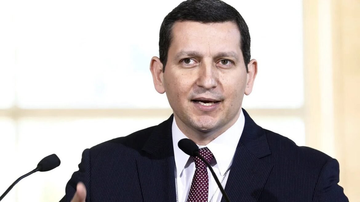 Man in a dark suit speaking into a microphone at a podium during a formal event