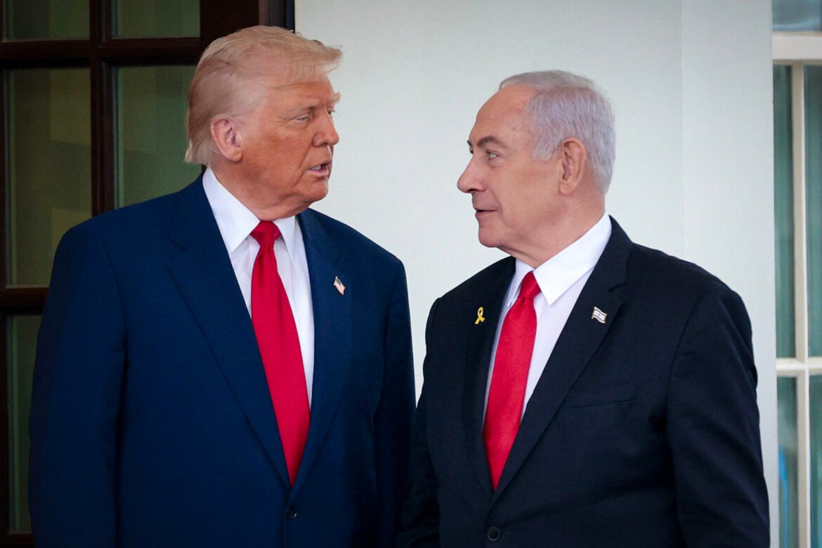 Two older men in dark suits with red ties talk closely on a light veranda, facing each other.