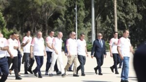 Group of Adults in White Shirts Walking in a Line Outdoors on a Sunny Day with Trees in the Background  Aleumumnews
