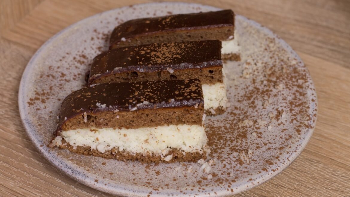 Slices of layered chocolate cheesecake on a speckled plate, with a glossy chocolate top and cocoa dusting on the plate Chocolate bar dessert with a creamy white filling, cut into parallel slices on a round ceramic plate A dessert plate featuring four rectangular chocolate-coated cake slices with a white cream middle, dusted with cocoa Rich chocolate dessert bars with a cream filling, arranged in a row on a light plate with cocoa powder sprinkled around Slice of chocolate mousse cake with white cream layer, served on a rustic plate with cocoa powder garnish