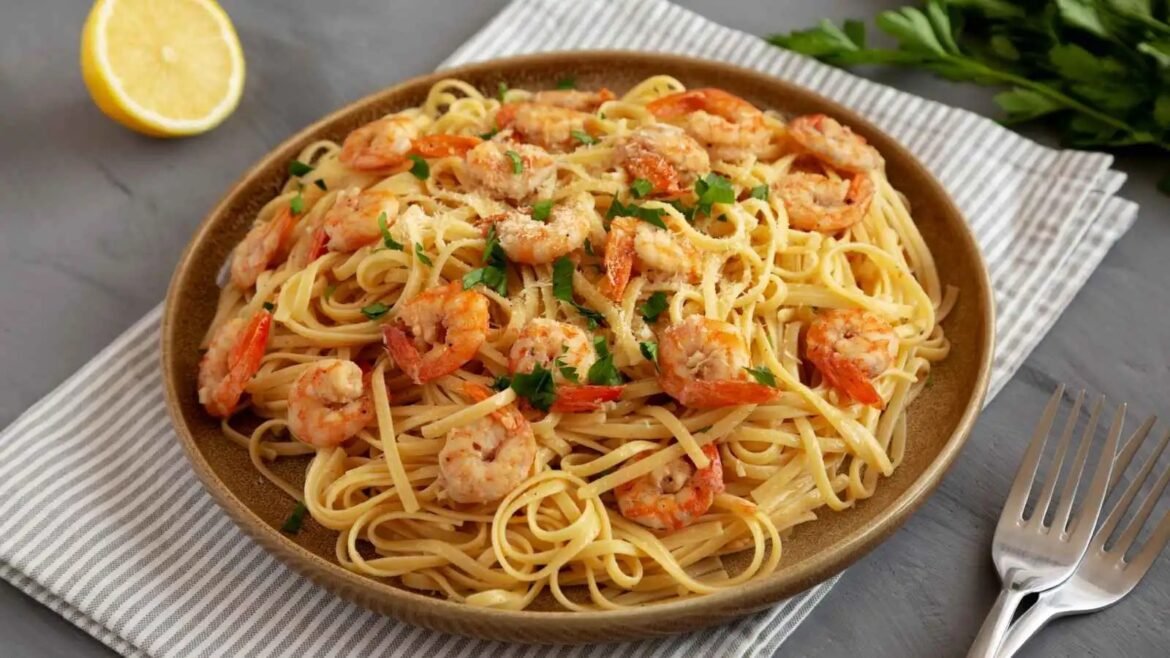 Linguine with shrimp in a creamy sauce, garnished with parsley, served in a brown bowl with a lemon half nearby on a striped napkin