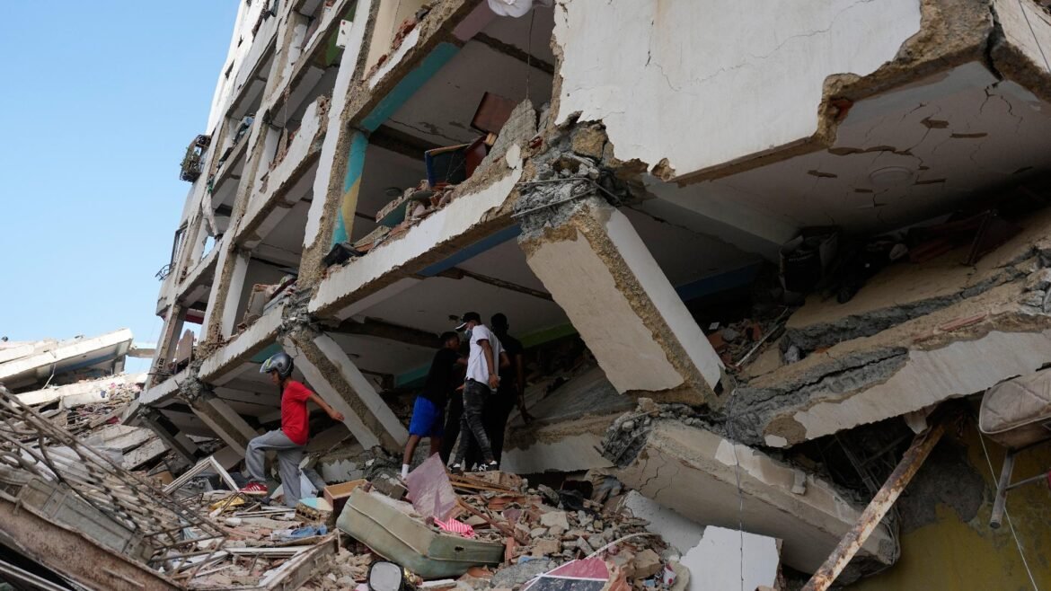 Collapsed multi-story building with exposed concrete and rubble; people search through the wreckage.