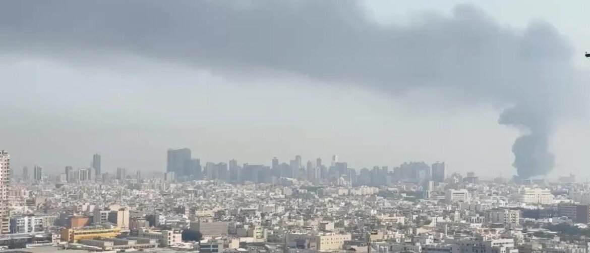 City skyline with a thick smoke plume rising from the right side over a dense urban area.