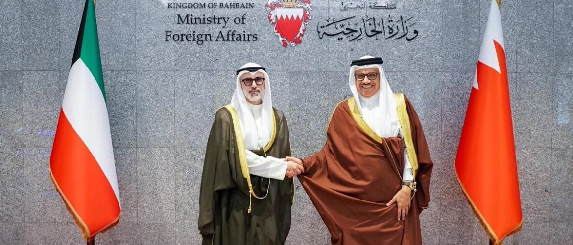 Two Bahraini officials in traditional robes shake hands in front of the Ministry of Foreign Affairs crest, flanked by national flags on both sides