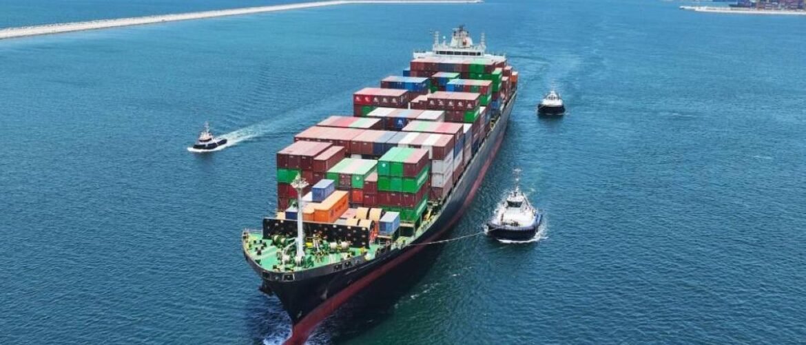 Large container ship escorted by three tugboats through calm blue sea, stacking colorful cargo containers on deck