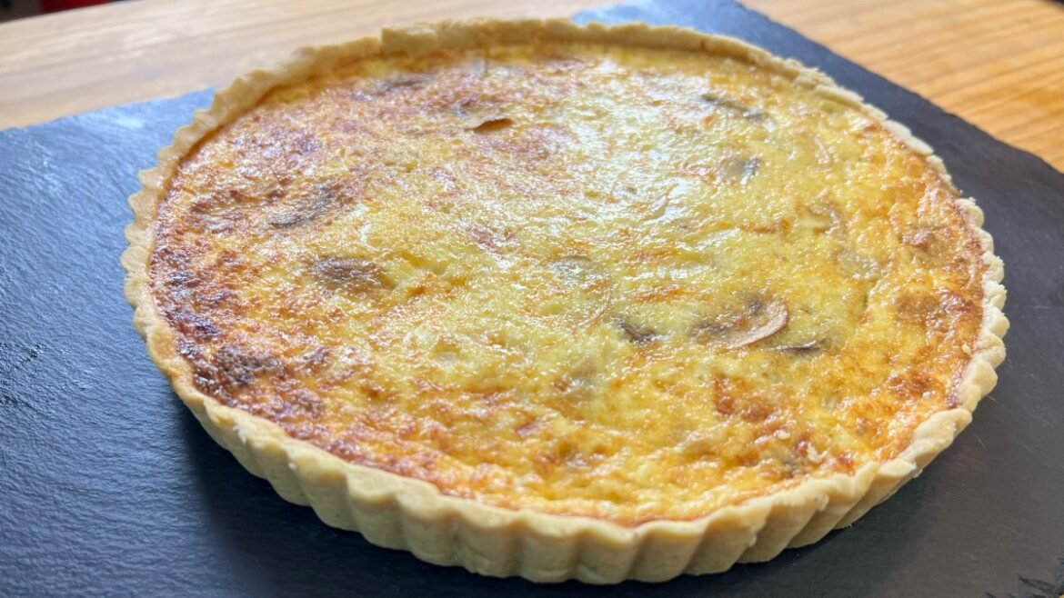 Quiche in a fluted crust on a dark slate board, golden-brown top crisp and cheesy