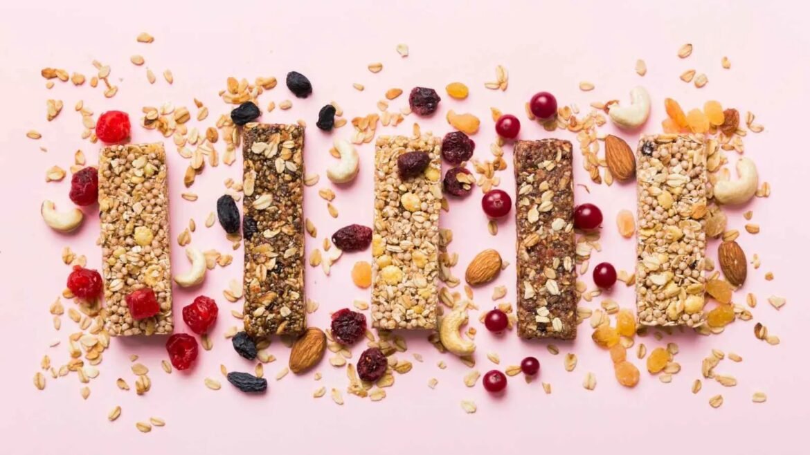 Row of six granola bars with oats, nuts, and dried fruits on a pink background.