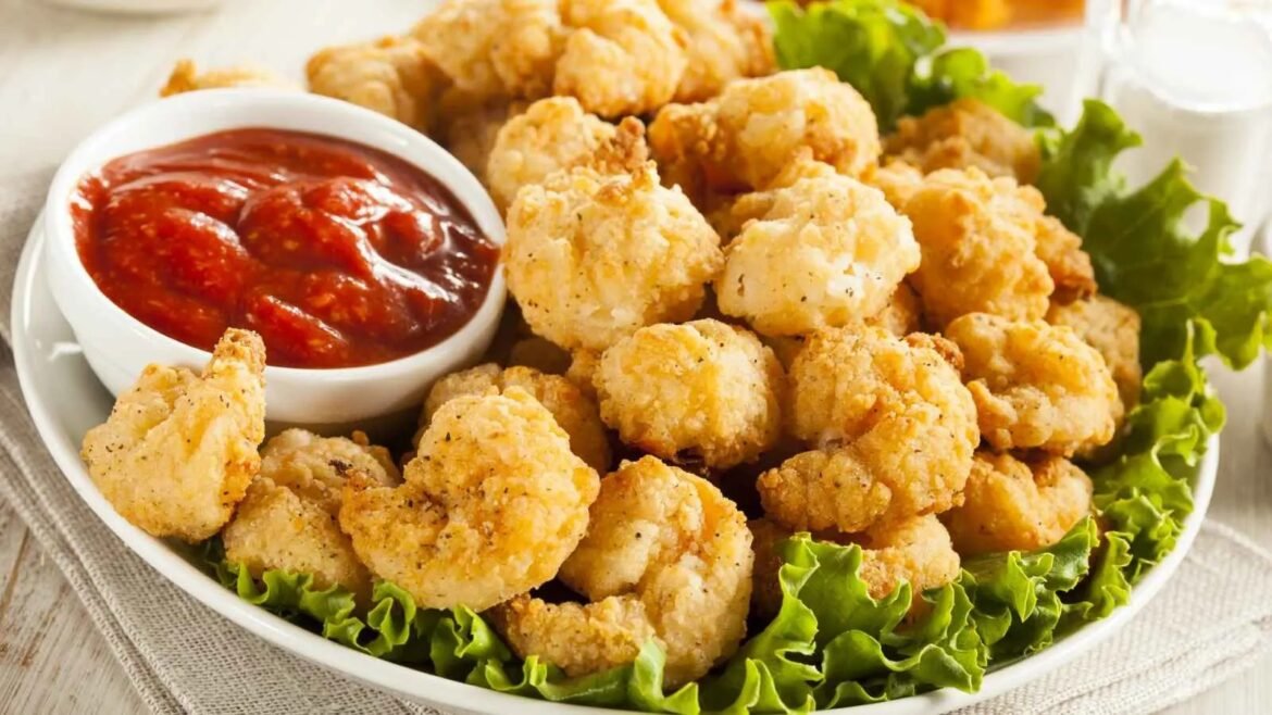 Golden fried chicken bites arranged on a bed of green lettuce with a side of red dipping sauce in a white bowl