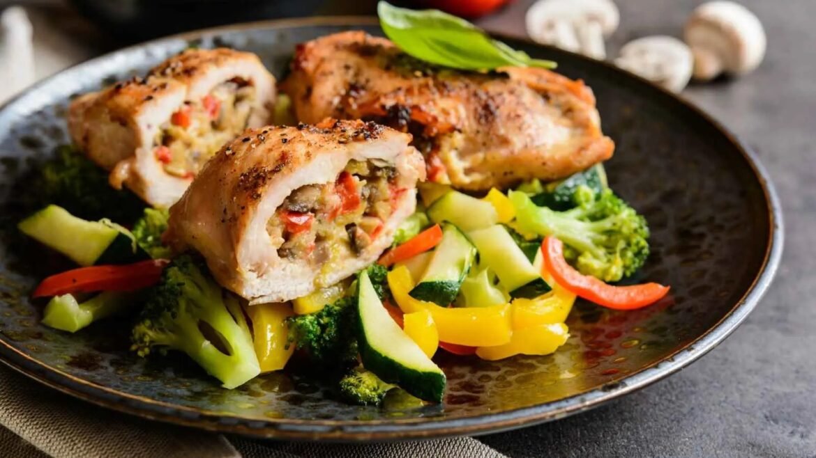 Sliced stuffed chicken breast with colorful diced vegetables on a dark plate, with broccoli and peppers nearby.
