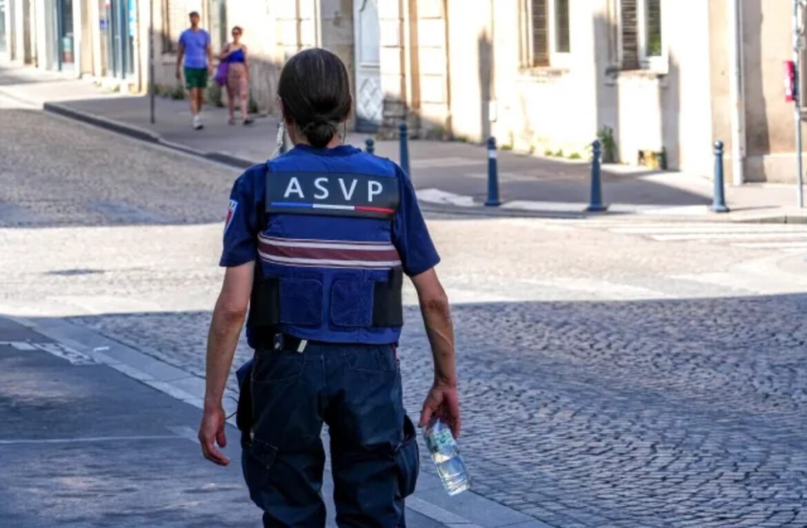 Person in a blue ASVP uniform walking away on a sunny cobblestone street, holding a water bottle