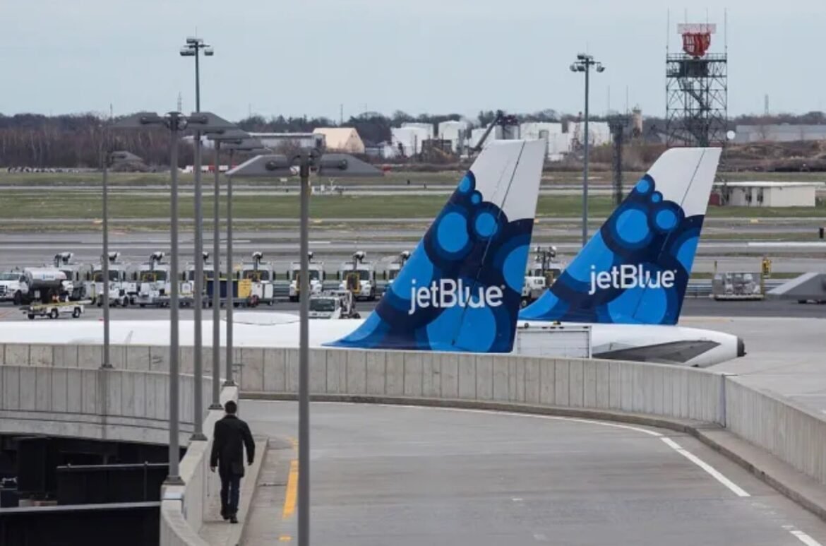 JetBlue airplane tails with blue bubble pattern at a terminal, a person walking along a ramp in the foreground.