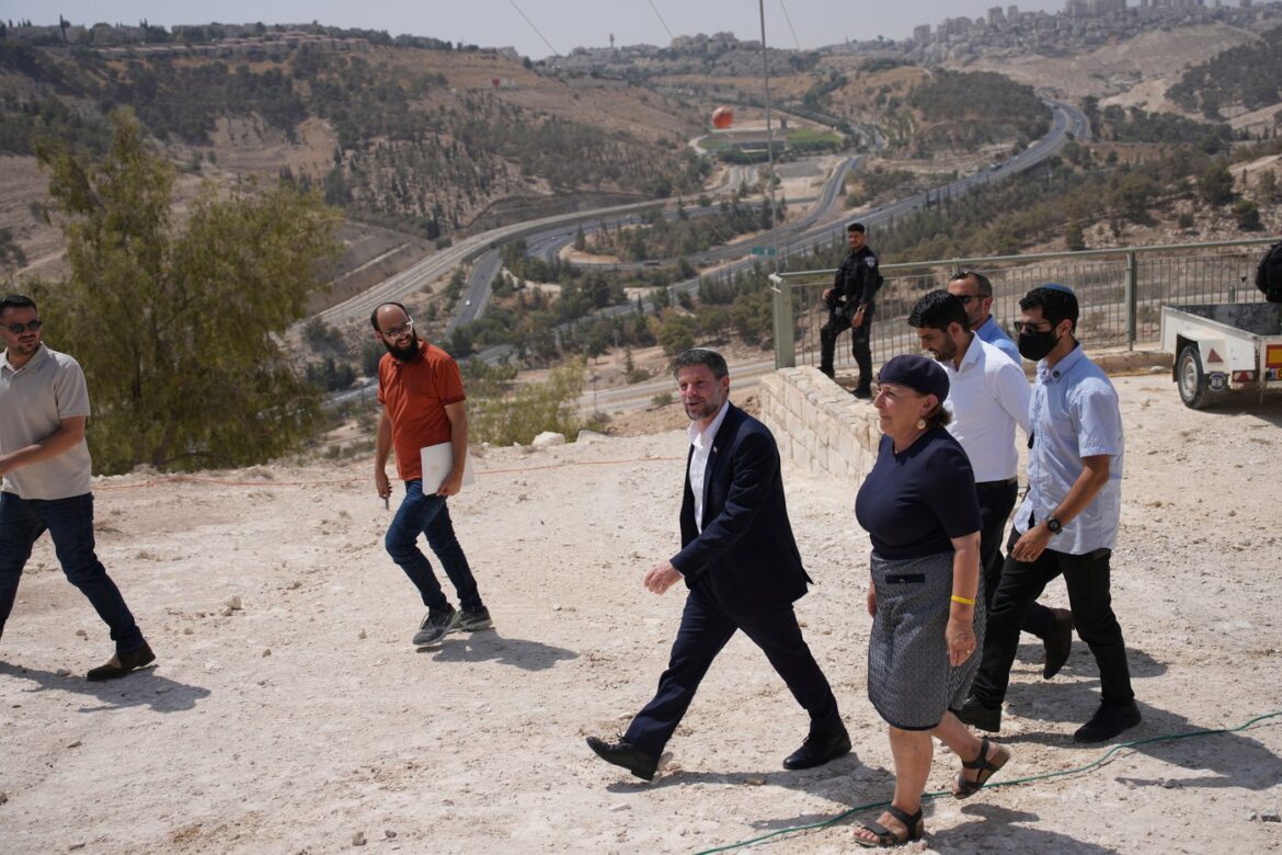 Group of professionals walking along a rocky overlook with a winding highway and hills in the background, during daytime