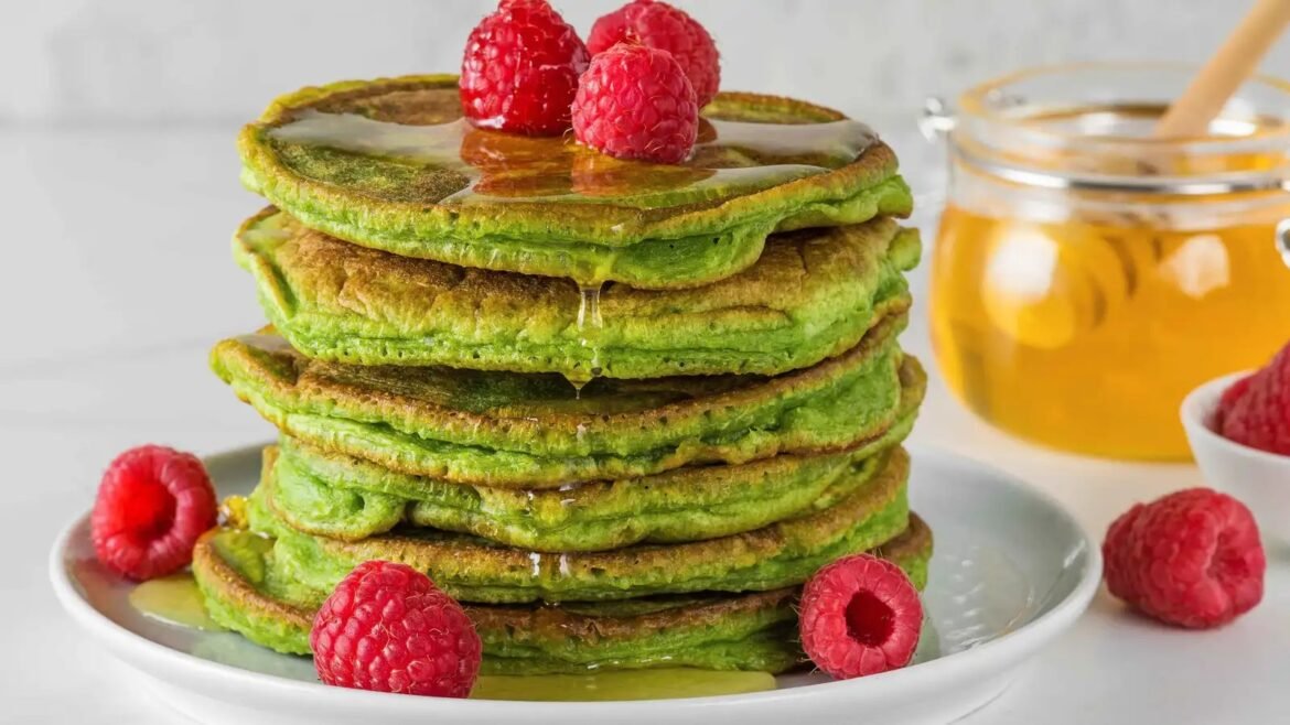 Stack of green matcha pancakes drizzled with honey, topped with raspberries on a white plate