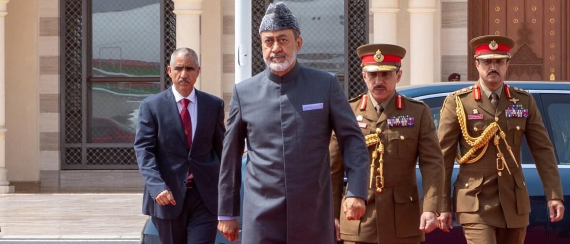 A man in a gray traditional outfit and cap walks with two uniformed officers in front of a building.