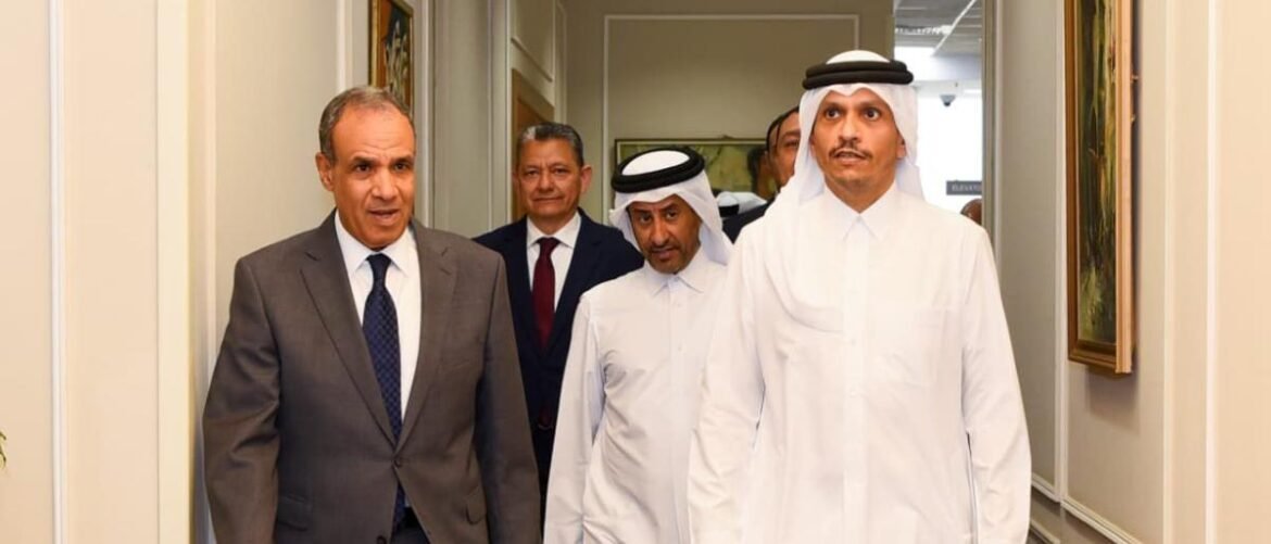 Group of men in a hallway: two in white thobes lead the way, one in a suit follows, a formal delegation walking together.