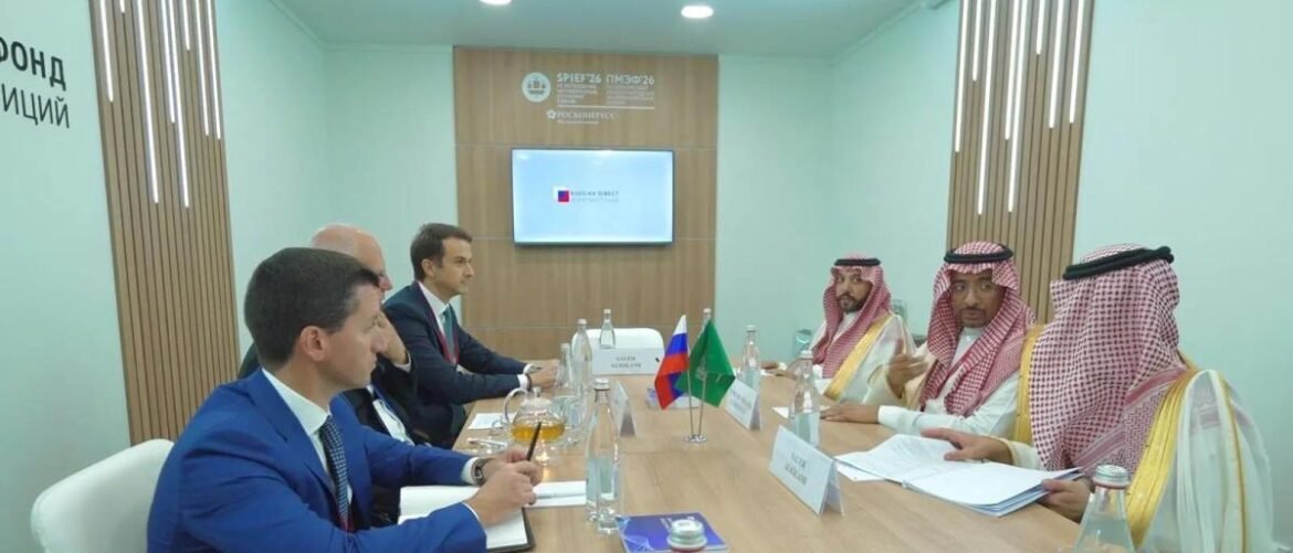 Group of men in suits and traditional robes sit around a conference table with flags, reviewing documents in a formal meeting.