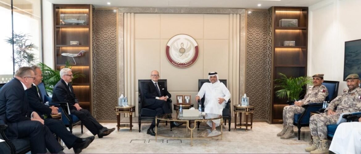 Formal meeting in a luxurious office: two men seated center in armchairs with officials on both sides, crest on the wall behind them and glass coffee table between them.