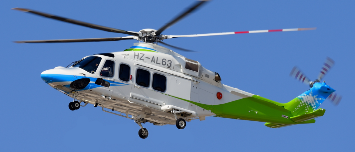 White helicopter with blue nose and green tail in mid‑flight against a clear blue sky, registration HZ-AL63.