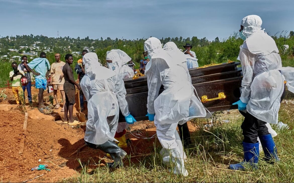 Healthcare workers in full protective suits carry a black coffin at a grave site, as locals watch in a rural area.
