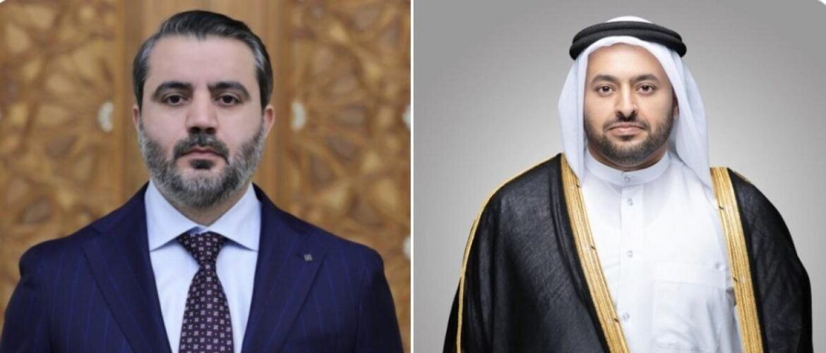 Two men side by side: on the left, a man in a navy pinstripe suit with a patterned tie; on the right, a man in a white thobe with a black-and-gold bisht and head covering.