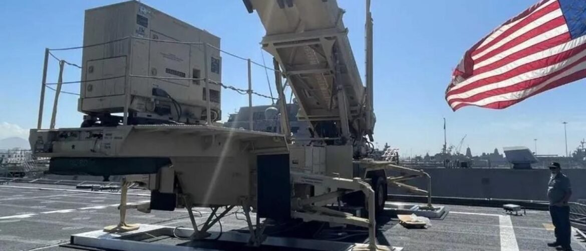 Missile launcher mounted on a naval deck with an American flag and a crew member standing nearby.
