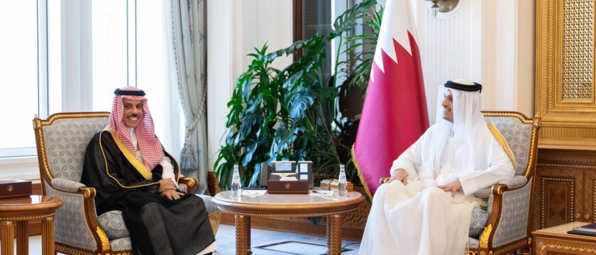 Two men in traditional attire sit in ornate chairs across from each other in a formal meeting room, Bahrain flag between them.