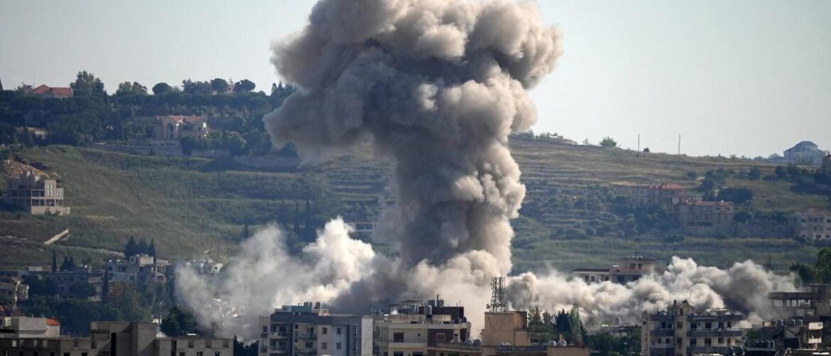 Large plume of smoke rising above a city after an explosion, with surrounding buildings and hills in the background.