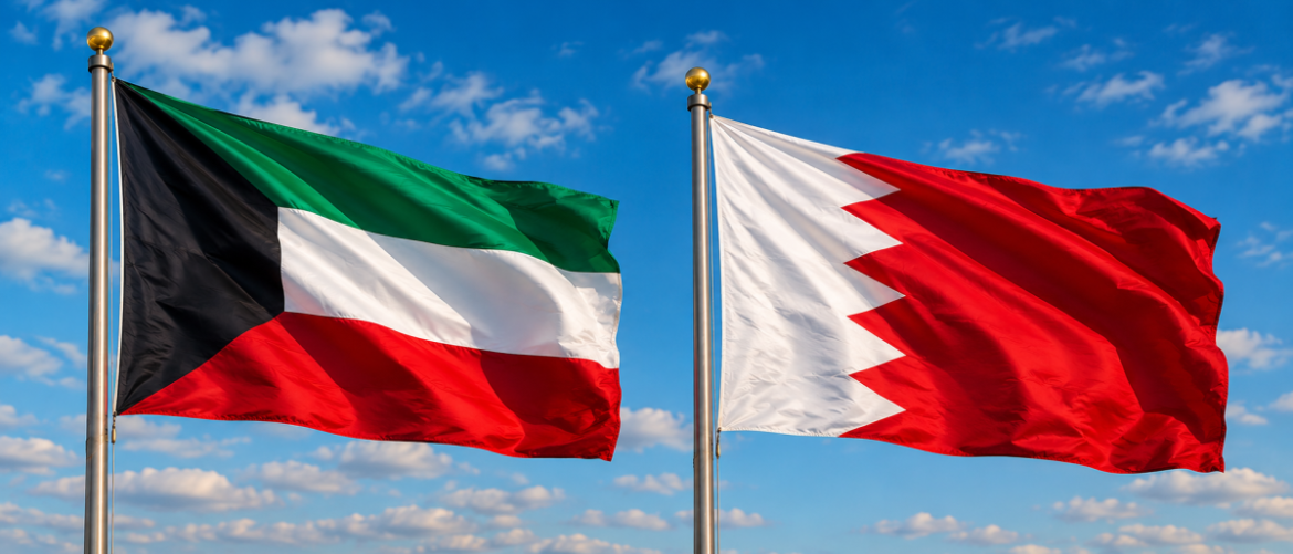 Two national flags flying side by side in the wind against a blue sky: Kuwait on the left and Bahrain on the right.