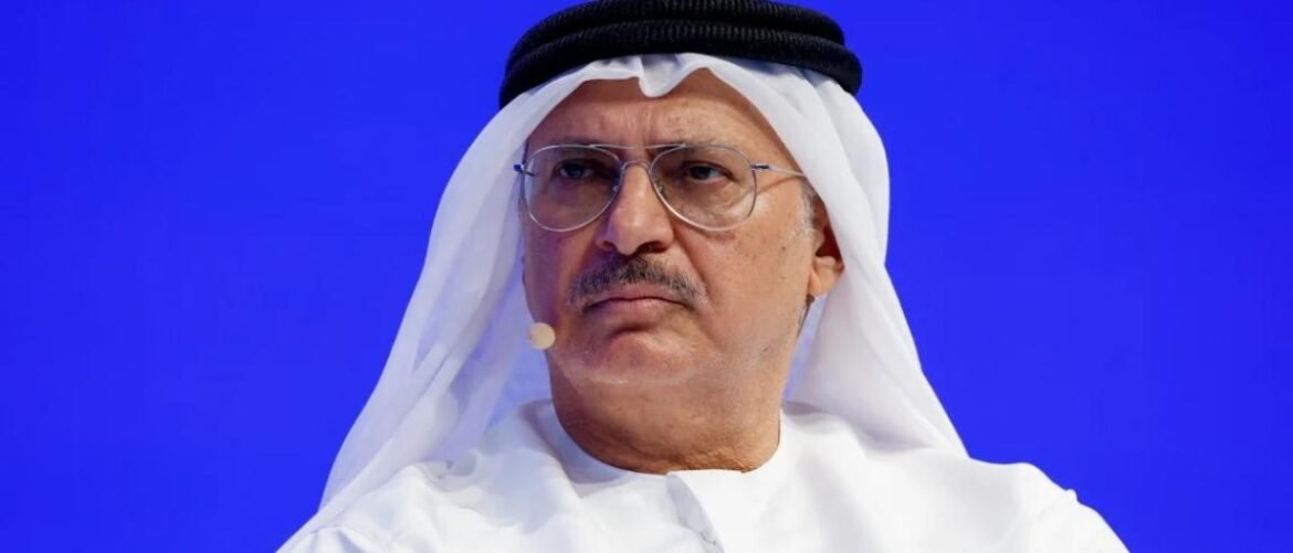Middle-aged man in a white kandura and ghutra with glasses speaking at a conference against a blue background.
