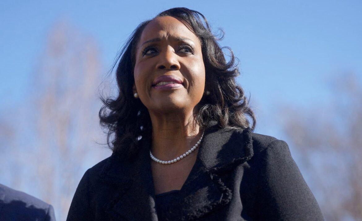 Portrait of a woman wearing a pearl necklace and dark blazer, looking upward against a clear blue sky.
