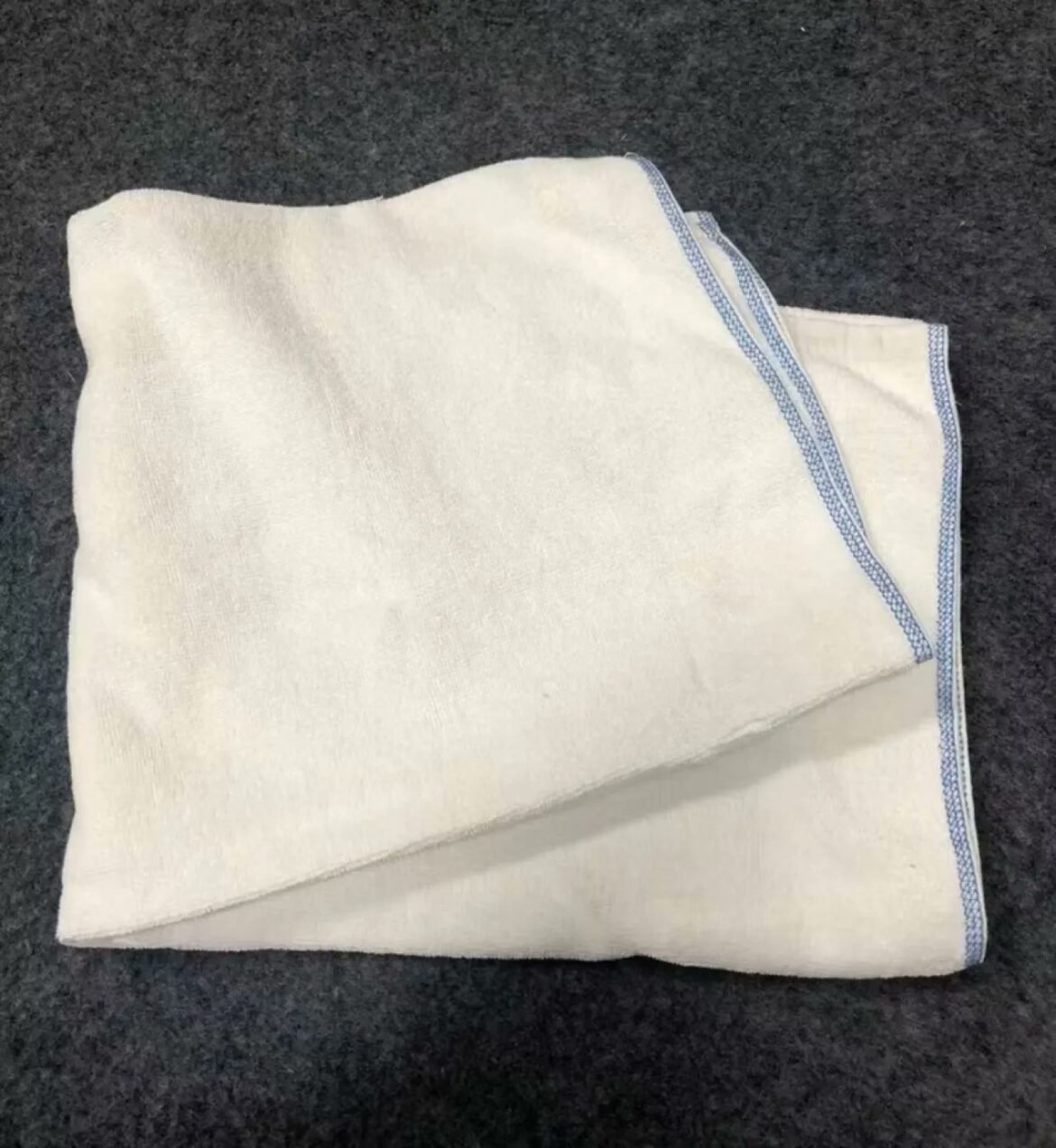Folded white linen napkin with blue embroidered border on a dark surface.