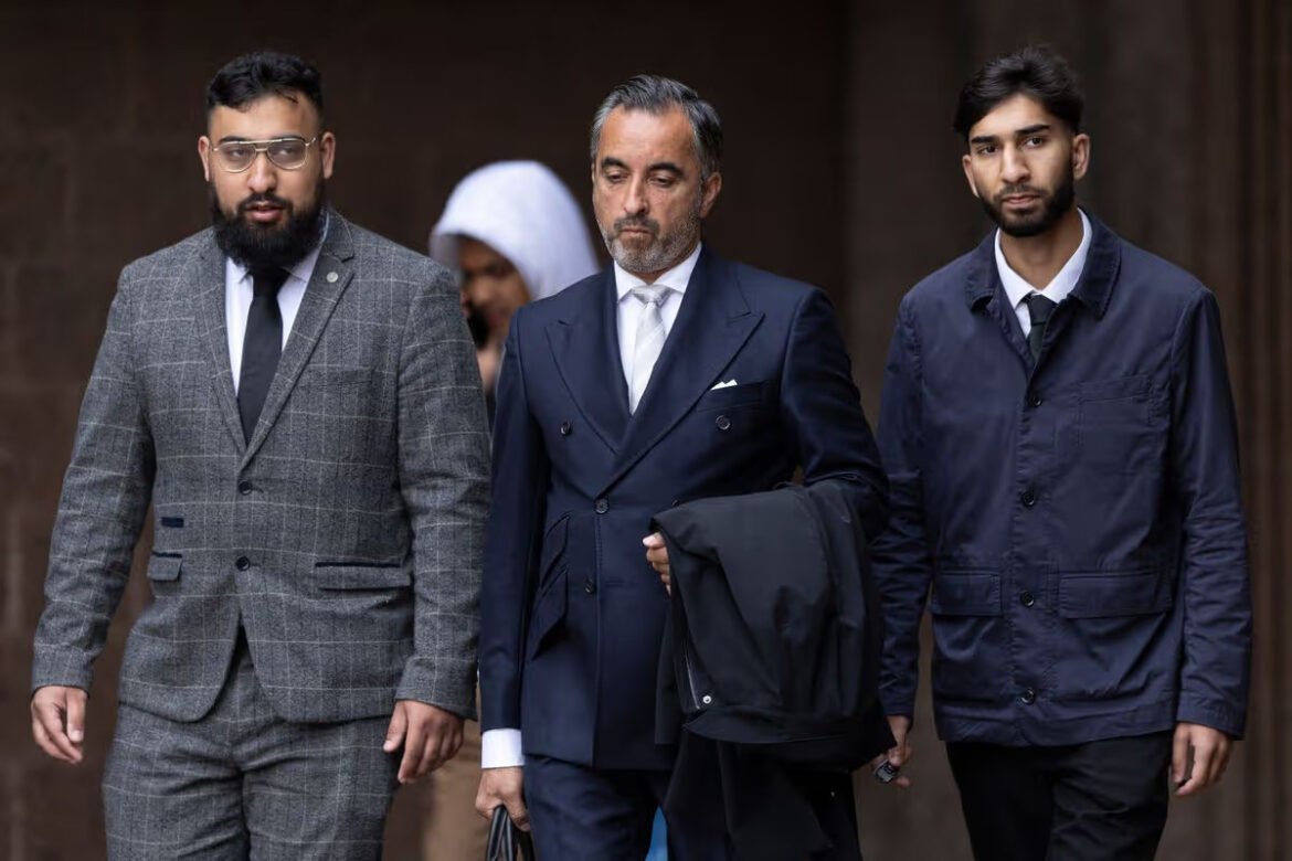 Three men in suits walk together outdoors; the middle man in a navy suit holds a coat and looks ahead.