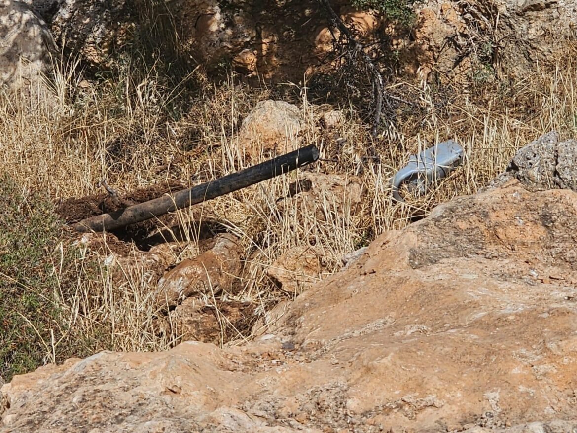 A weathered black pipe resting on dry grass and rocky hillside.
