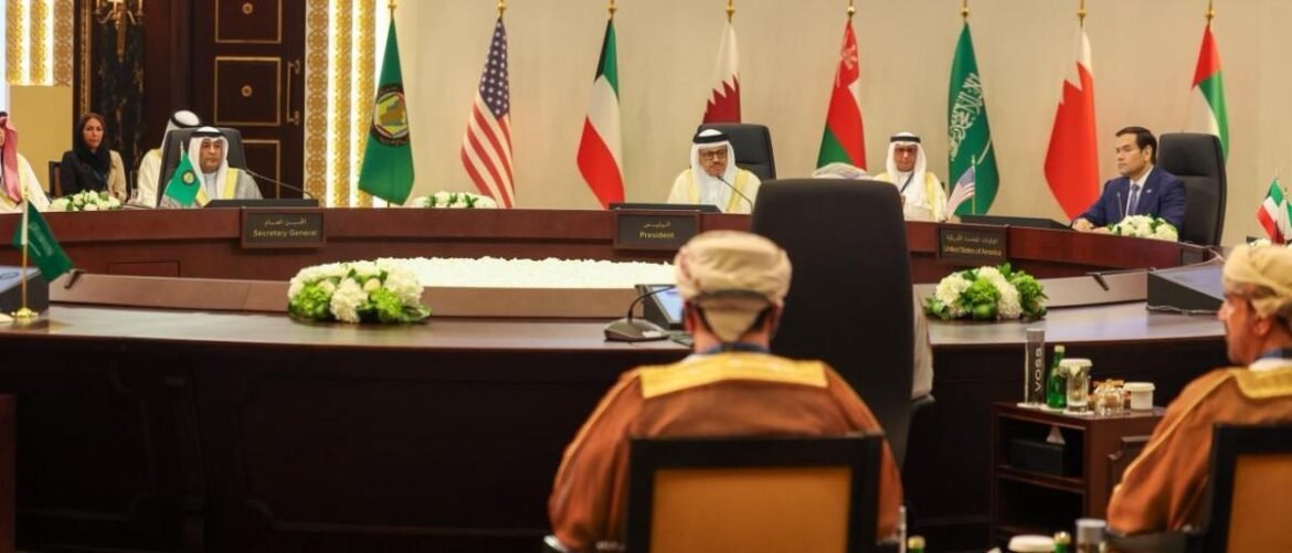 Diplomatic leaders sit around a large curved conference table with multiple national flags behind them, including the U.S. and Gulf states, as a formal summit takes place; nameplates read 'President' and 'Secretary General' at the front.