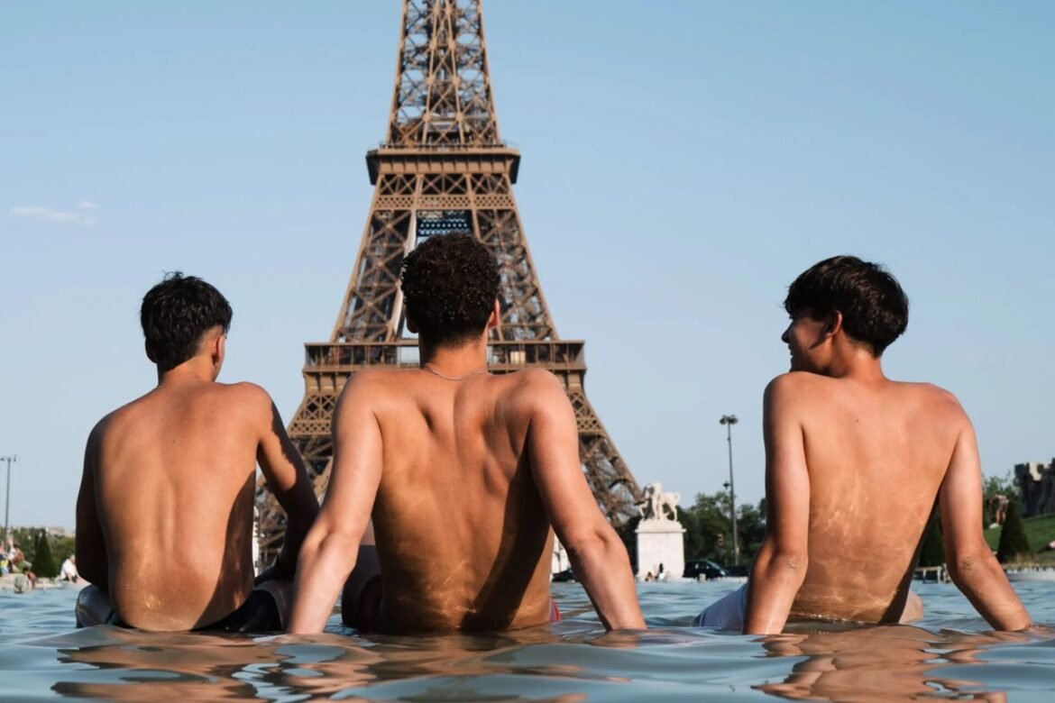 Three shirtless men sit with their backs to the camera in a pool, Eiffel Tower visible in the background.