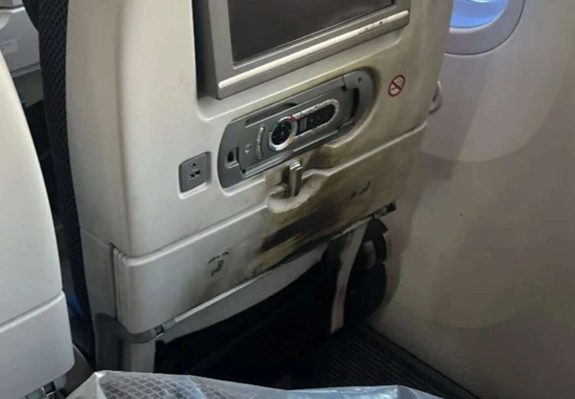 Airline seat back with an in-seat entertainment screen and control panel on a gray tray area.