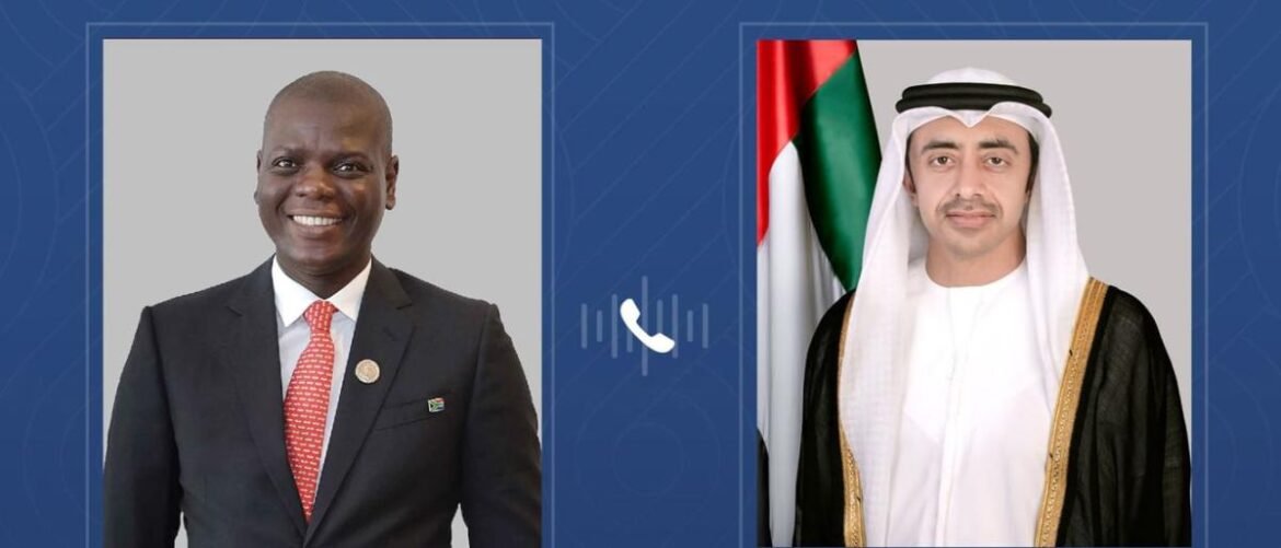 Two men in portrait frames: left is a smiling Black man in a dark suit and red tie; right is a man in traditional white robe with a black cloak and UAE flag behind him. A phone icon sits between them.