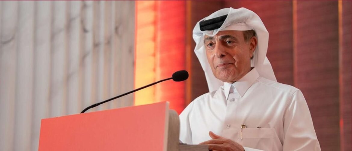 Elderly man in a white thobe and headscarf delivers a speech at a podium with a microphone.
