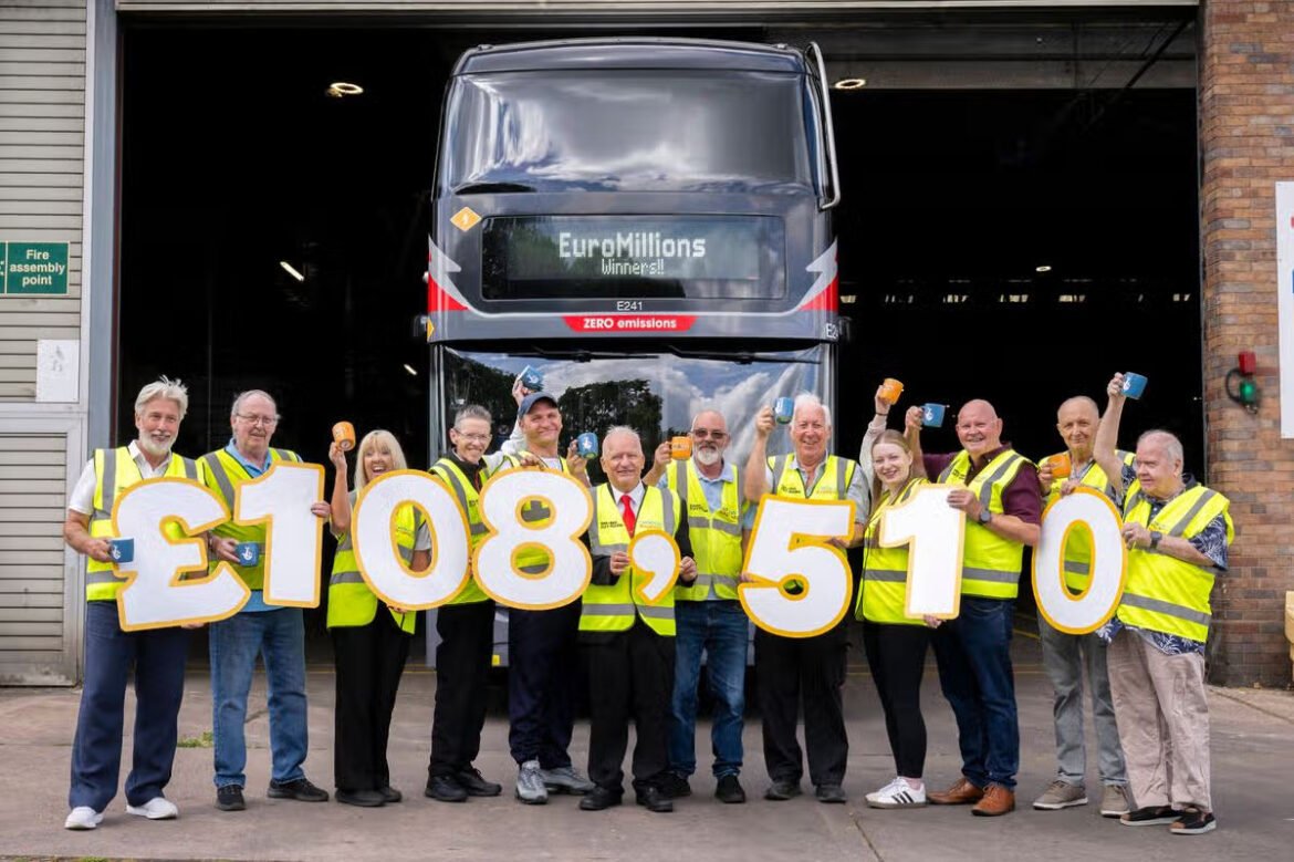 Group of people in yellow safety vests holding oversized digits spelling £108,510 in front of a truck, celebrating a fundraising total at a depot/wash area.