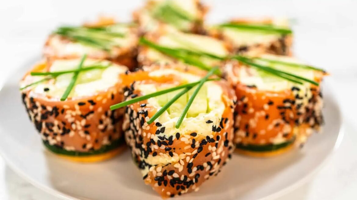 Salmon-topped sesame rolls with cucumber and avocado, sprinkled with black and white sesame seeds on a white plate.