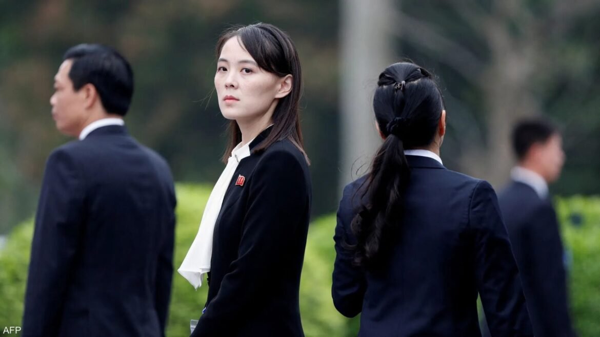 Woman in a black blazer and white blouse stands outdoors among colleagues in suits, looking toward the camera (center).